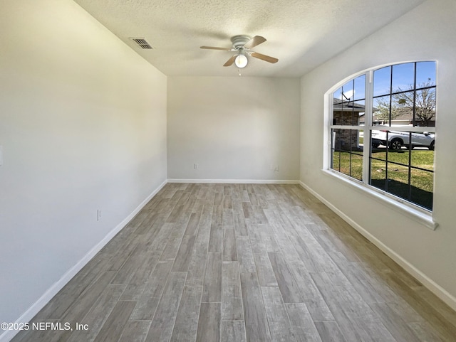 empty room with visible vents, a textured ceiling, baseboards, and wood finished floors