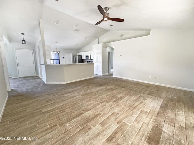 unfurnished living room with wood finished floors, ceiling fan with notable chandelier, baseboards, and lofted ceiling