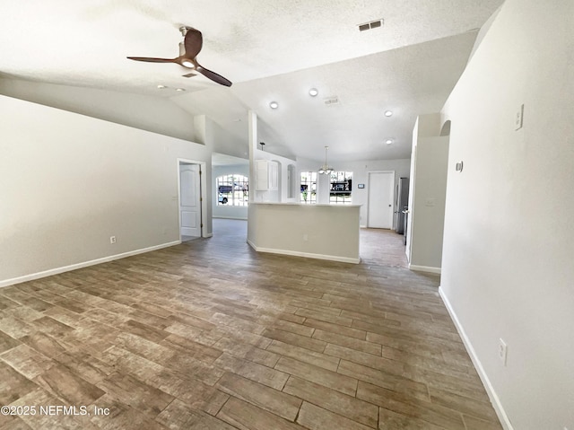 unfurnished living room with wood finished floors, baseboards, visible vents, vaulted ceiling, and ceiling fan with notable chandelier