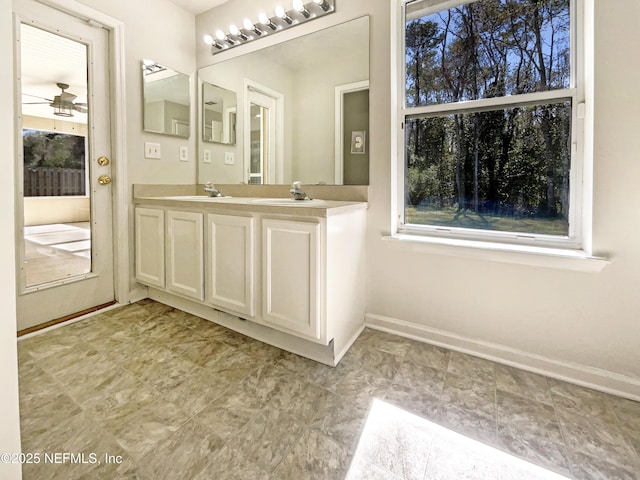 bathroom with a sink, baseboards, a ceiling fan, and double vanity