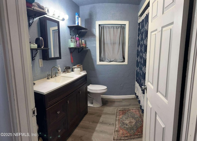 bathroom featuring toilet, wood finished floors, baseboards, vanity, and a textured wall