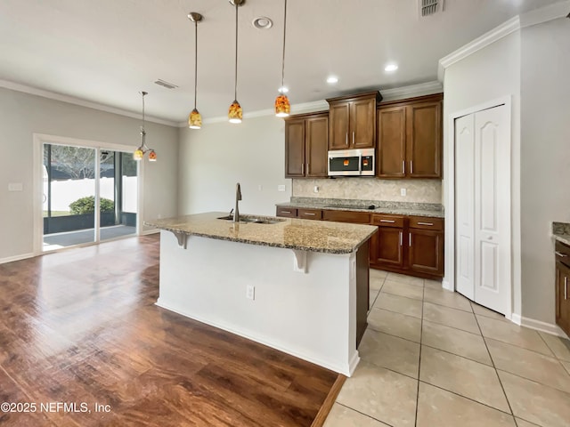 kitchen with a sink, stainless steel microwave, backsplash, stone counters, and black electric cooktop