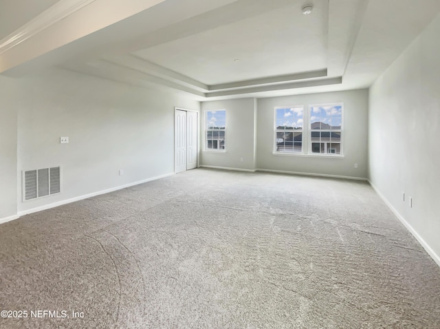 carpeted spare room with visible vents, a raised ceiling, and baseboards