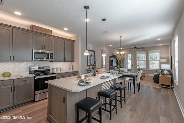 kitchen featuring a sink, open floor plan, dark brown cabinets, appliances with stainless steel finishes, and tasteful backsplash