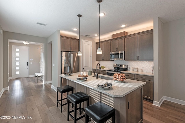 kitchen with a kitchen bar, visible vents, a sink, tasteful backsplash, and stainless steel appliances