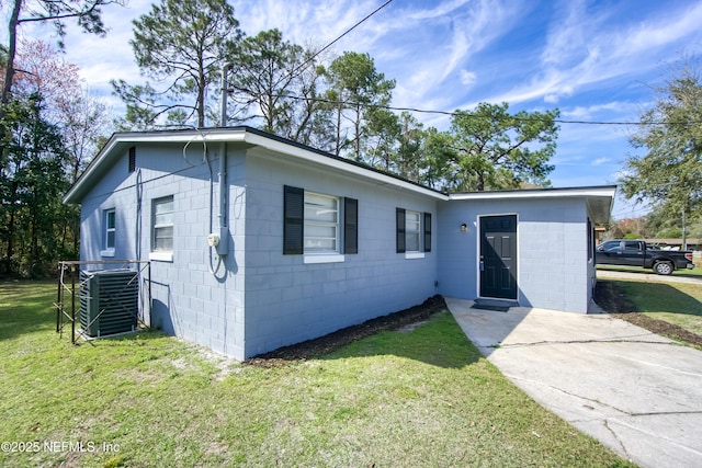 single story home with central AC unit, concrete block siding, and a front lawn