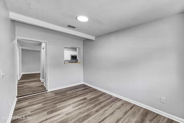 spare room with visible vents, a textured ceiling, baseboards, and wood finished floors