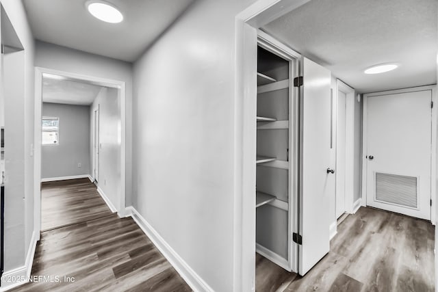 corridor with visible vents, a textured ceiling, baseboards, and wood finished floors