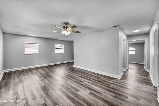 empty room with visible vents, baseboards, ceiling fan, and dark wood-style flooring