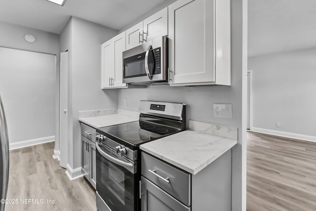 kitchen featuring white cabinets, stainless steel appliances, light wood-type flooring, and baseboards