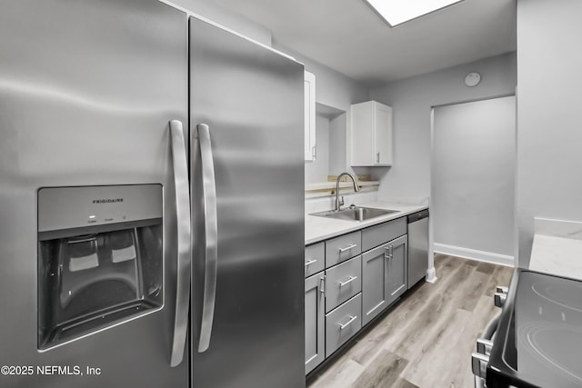 kitchen with a sink, gray cabinetry, light countertops, stainless steel appliances, and light wood-type flooring