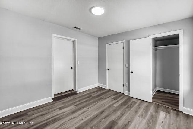 unfurnished bedroom with a closet, visible vents, baseboards, and wood finished floors