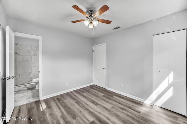 unfurnished bedroom featuring visible vents, ensuite bath, wood finished floors, a closet, and baseboards