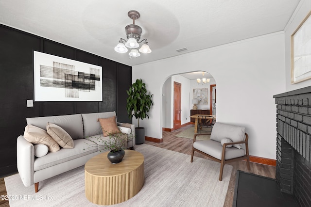 living area featuring light wood-type flooring, visible vents, a notable chandelier, arched walkways, and a brick fireplace