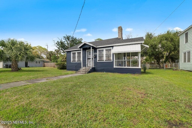 view of front of home with a chimney, roof with shingles, a front yard, and fence