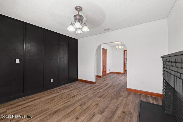 unfurnished living room with visible vents, a notable chandelier, wood finished floors, arched walkways, and a brick fireplace