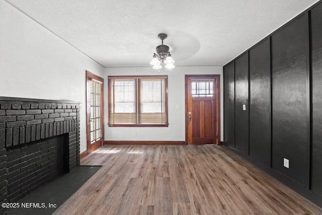 unfurnished living room featuring ceiling fan, a brick fireplace, wood finished floors, and a textured ceiling