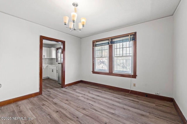 empty room featuring baseboards, light wood-type flooring, plenty of natural light, and an inviting chandelier