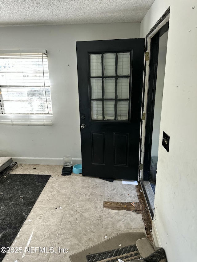 doorway to outside with a textured ceiling and baseboards