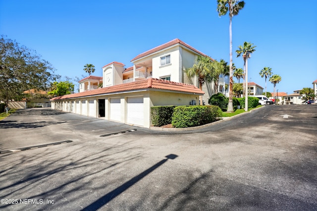 exterior space with community garages, a tile roof, and stucco siding