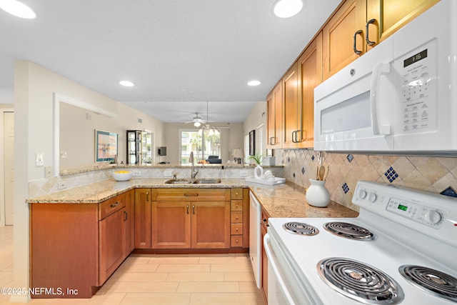 kitchen with light stone countertops, brown cabinets, a peninsula, white appliances, and a sink