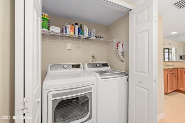 clothes washing area with washer and clothes dryer, laundry area, light wood finished floors, and visible vents