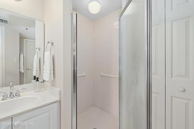 full bathroom with visible vents, a textured ceiling, a shower stall, vanity, and a textured wall