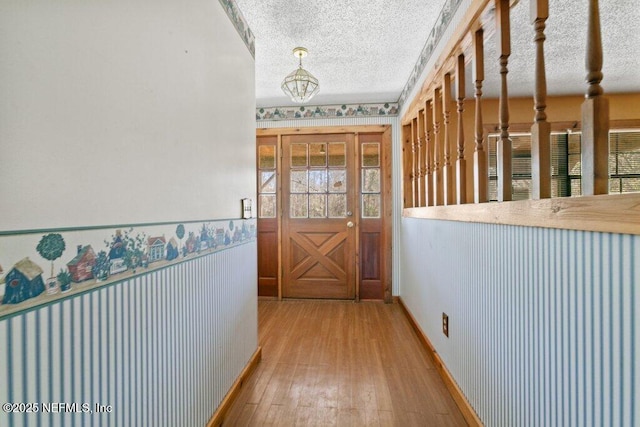 hall featuring wood-type flooring, a textured ceiling, and wainscoting