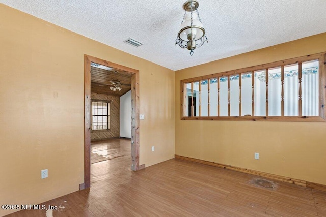 spare room featuring visible vents, baseboards, a textured ceiling, and wood finished floors