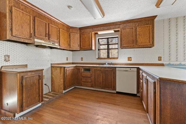 kitchen with under cabinet range hood, brown cabinets, dishwasher, and wallpapered walls