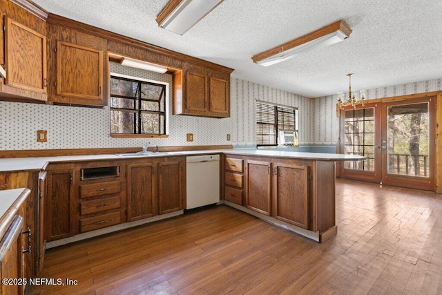 kitchen featuring dark wood-style floors, wallpapered walls, a peninsula, a sink, and dishwasher