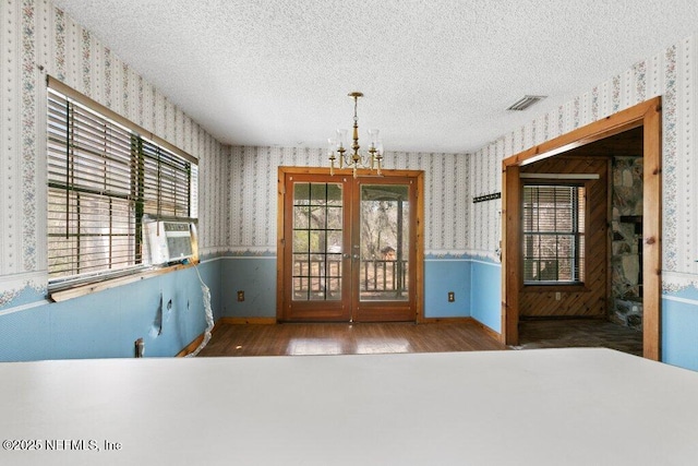 unfurnished dining area with a wainscoted wall, a textured ceiling, wallpapered walls, and visible vents