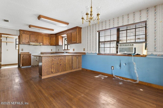 kitchen with visible vents, brown cabinets, under cabinet range hood, a textured ceiling, and wallpapered walls