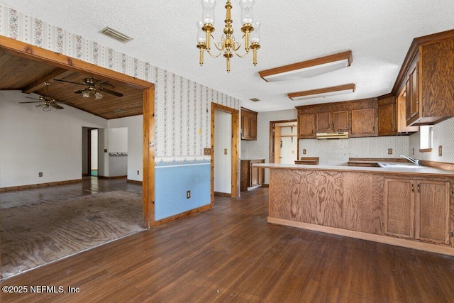 kitchen with visible vents, wallpapered walls, a peninsula, dark wood-style flooring, and a sink