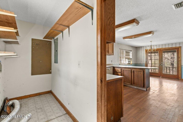 kitchen with visible vents, brown cabinets, a textured ceiling, a peninsula, and baseboards