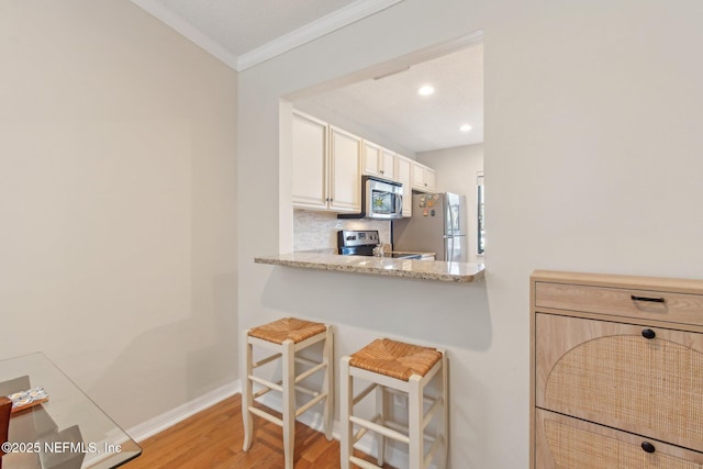 kitchen with light wood-style flooring, stainless steel appliances, crown molding, a kitchen breakfast bar, and tasteful backsplash