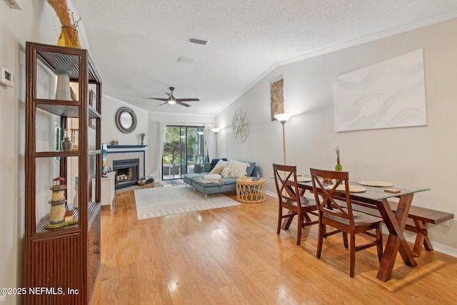 dining room with visible vents, ceiling fan, ornamental molding, a textured ceiling, and light wood-type flooring