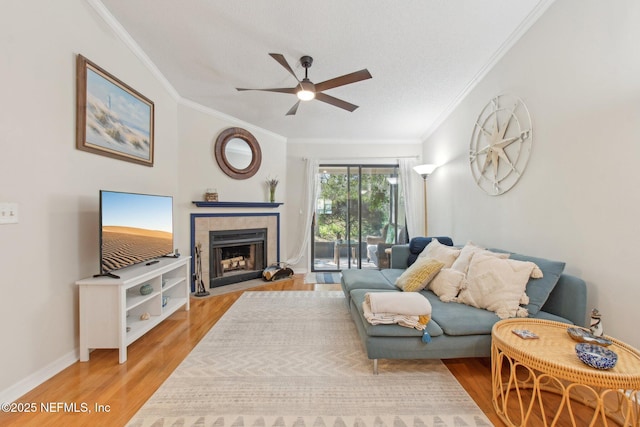 living area with a tiled fireplace, light wood-type flooring, ceiling fan, and ornamental molding