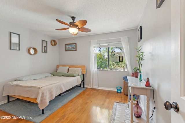 bedroom featuring ceiling fan, baseboards, a textured ceiling, and light wood-style flooring