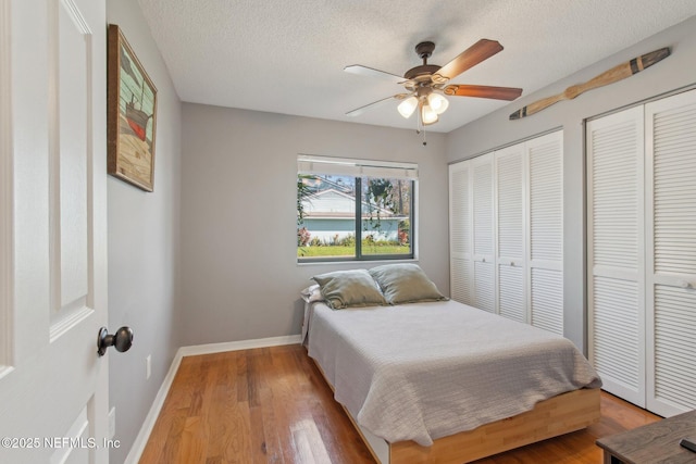 bedroom with ceiling fan, baseboards, multiple closets, wood finished floors, and a textured ceiling