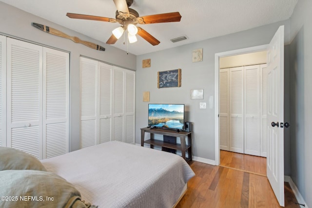 bedroom featuring hardwood / wood-style floors, baseboards, visible vents, ceiling fan, and two closets