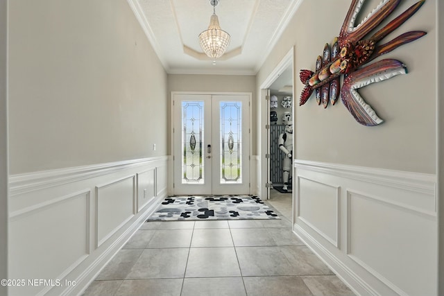 entryway with a tray ceiling, crown molding, a decorative wall, and french doors