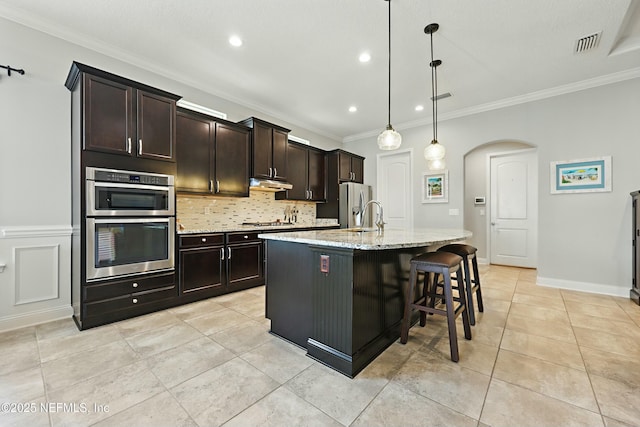 kitchen featuring visible vents, backsplash, under cabinet range hood, arched walkways, and stainless steel appliances