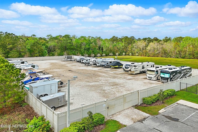 uncovered parking lot featuring a view of trees and fence