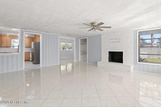 unfurnished living room with a ceiling fan, light tile patterned floors, a fireplace, and a textured ceiling