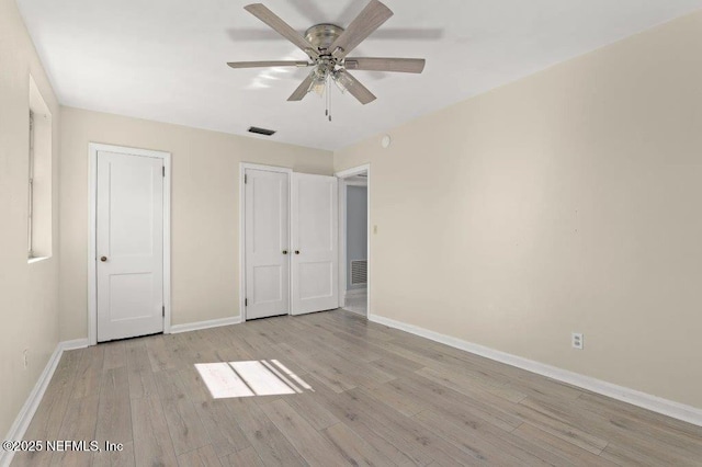 unfurnished bedroom featuring two closets, visible vents, baseboards, and light wood-style floors