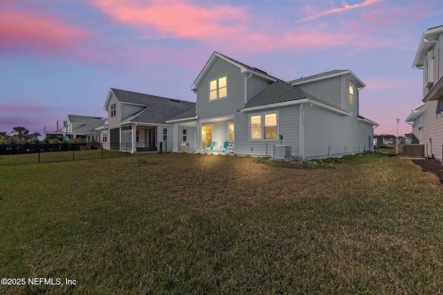 rear view of property with fence, a lawn, and central AC