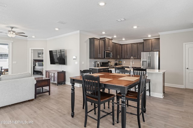 dining room featuring baseboards, light wood-style floors, ornamental molding, and a textured ceiling