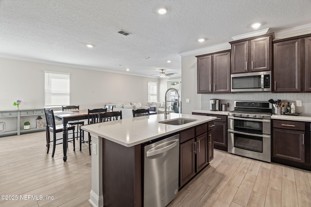 kitchen with light wood finished floors, a sink, decorative backsplash, light countertops, and appliances with stainless steel finishes