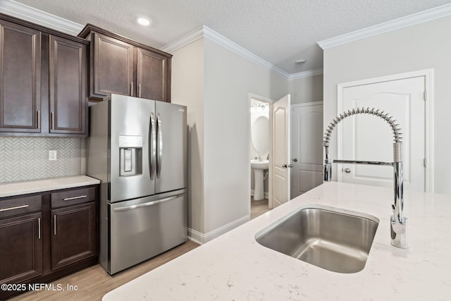 kitchen with light stone countertops, light wood-style flooring, a sink, dark brown cabinets, and stainless steel refrigerator with ice dispenser